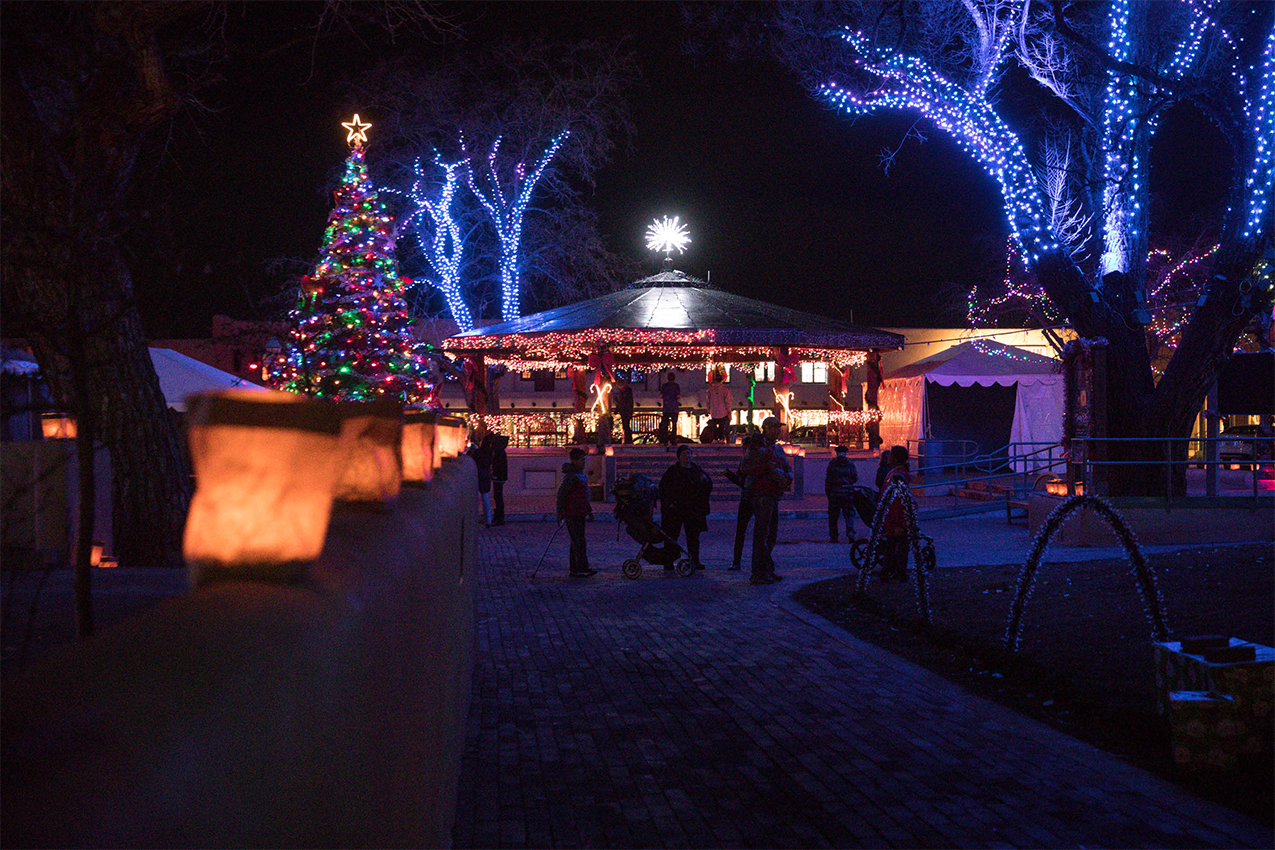 People standing in a square with trees and a gazebo lit up in colorful holiday lights.