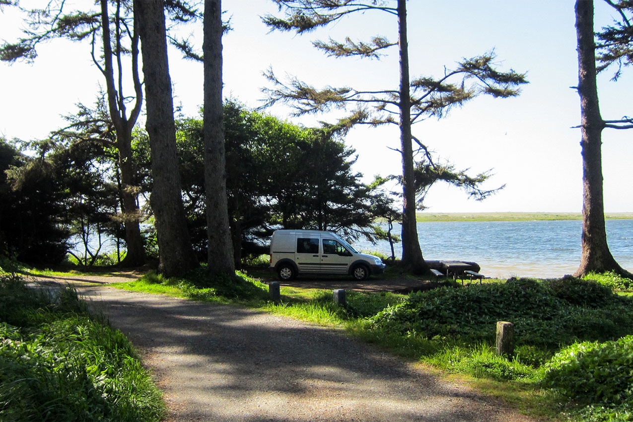 Van parked in the forest overlooking the ocean.