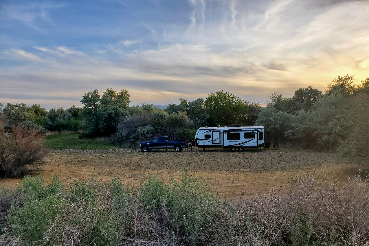 RV and trailer camped in an open field surrounded by trees.