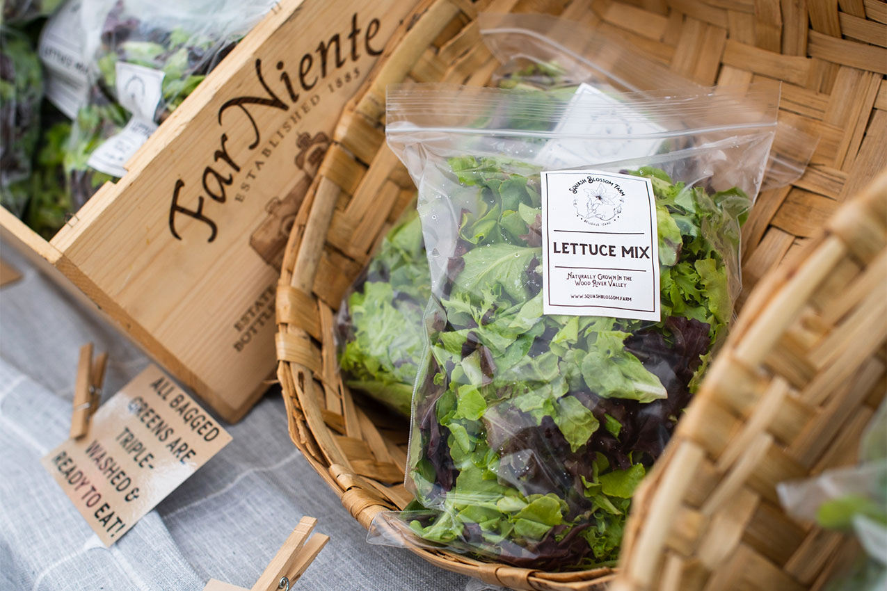 Bags of fresh lettuce in a basket on a table at a farmer's market.