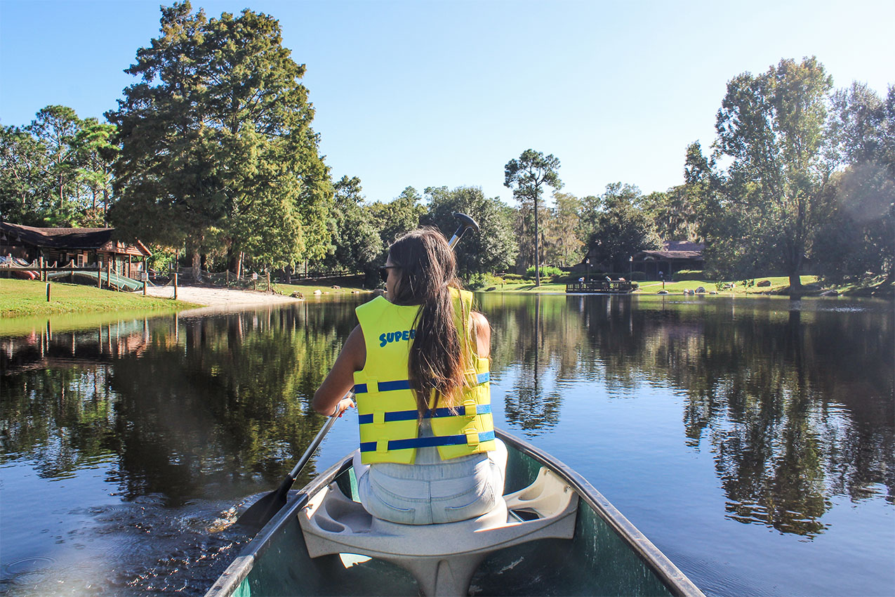 Woman wearing a life vest paddling a canoe on a lake.