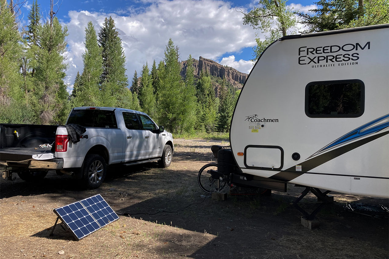 Solar panel in the sun next to a truck and RV with mountains in the back.