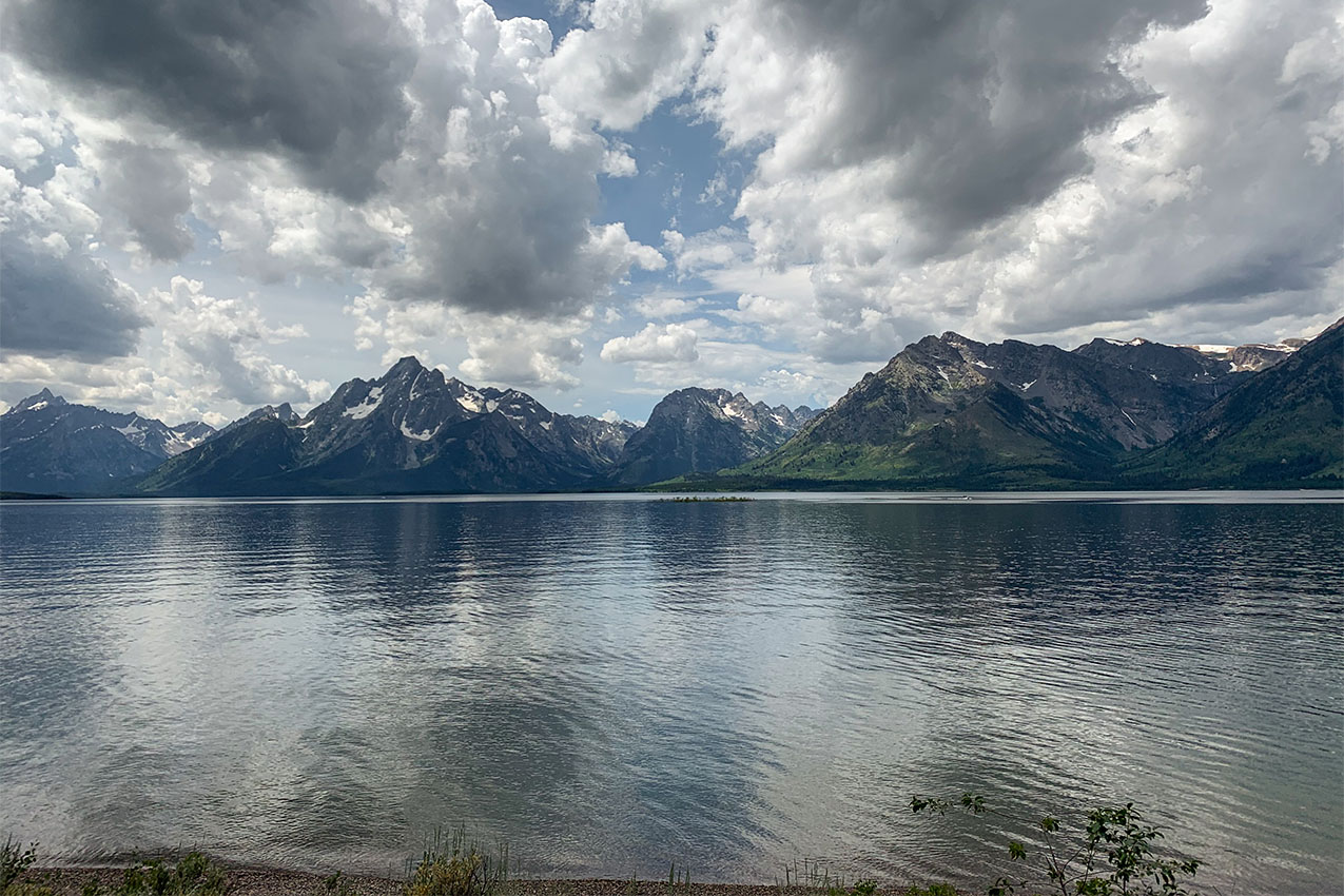 Teton Mountains on the edge of a lake under a cloud covered sky.