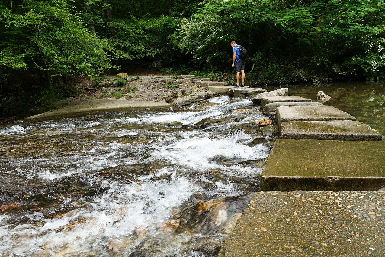 A man walking over a stone pathway across a creek.