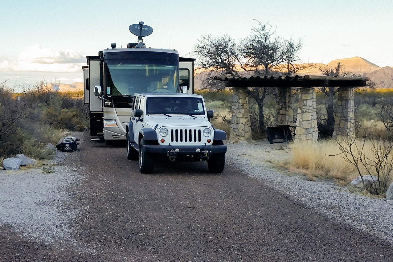 Jeep parked in front of a class A next to a stone picnic shelter.