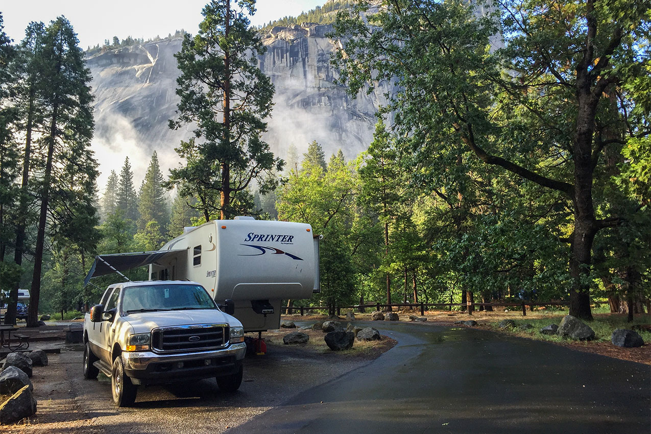 Truck and fifth wheel parked in a campground in front of mist covered mountains.