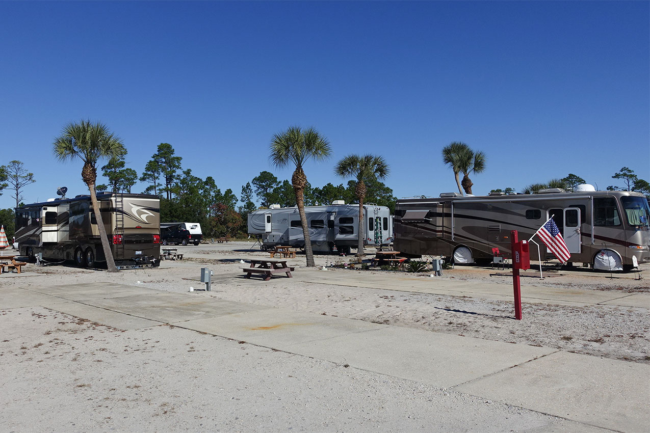 Concrete path leading towards several large RVs parked in sandy campsites.