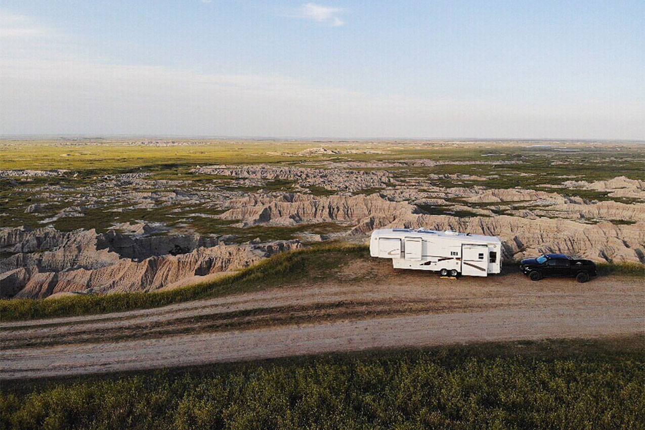 Lone RV and truck parked off the side of a dirt road overlooking geological features.