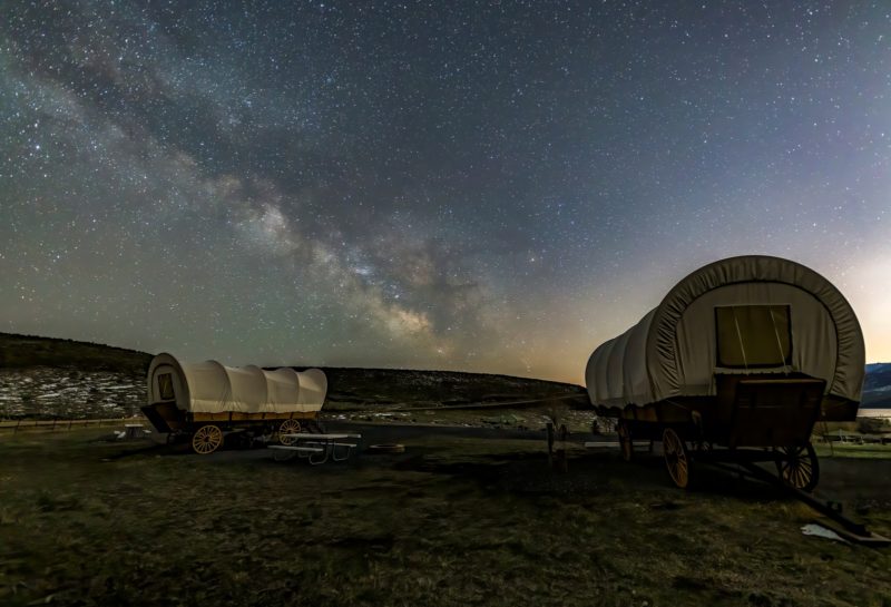 Two covered wagons parked under a dark, starry sky
