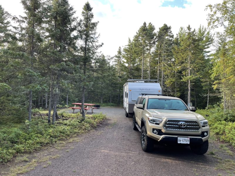 SUV towing trailer at gravel campsite in wooded area