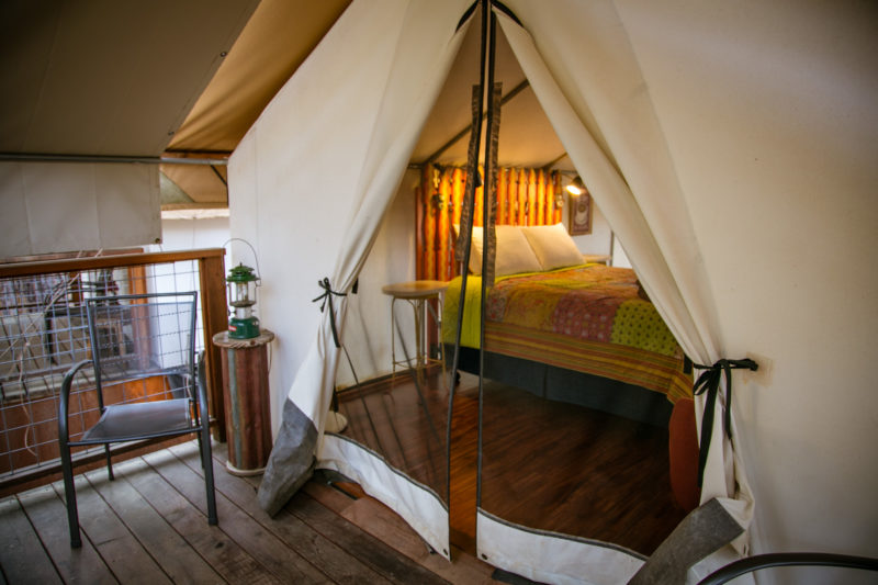 a canvas glamping tent with a bed and wooden floor