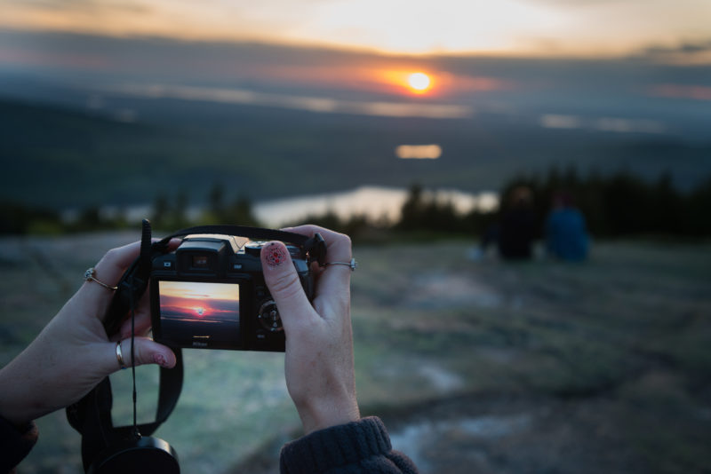 Woman taking photo with professional camera of sunrise over a mountain