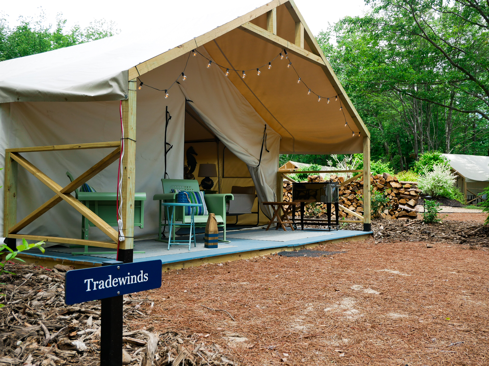 The exterior front porch of a safari glamping tent, with a small sign that reads "Tradewinds"
