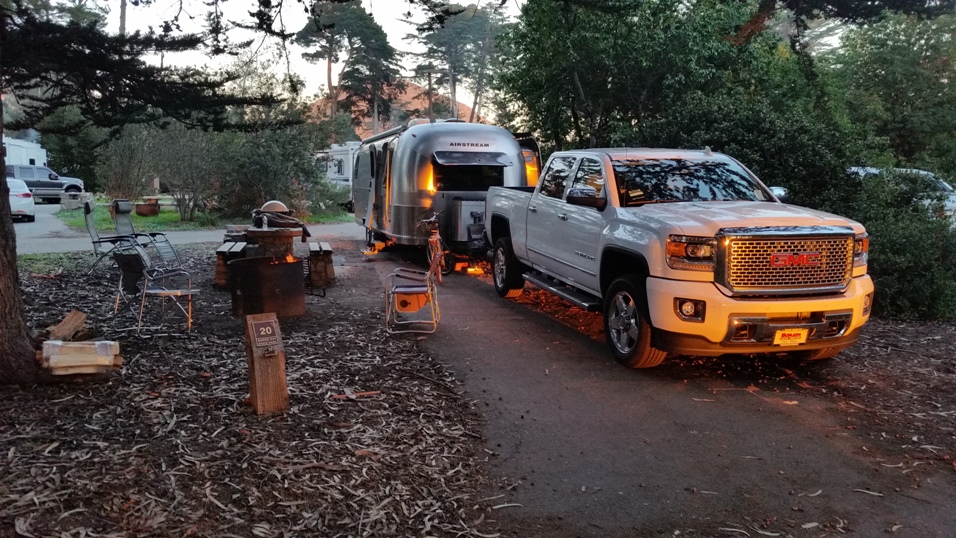 A truck and an Airstream trailer parked at a campsite during dusk