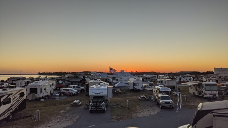 Several RVs parked at a campground at sunset with water in the background