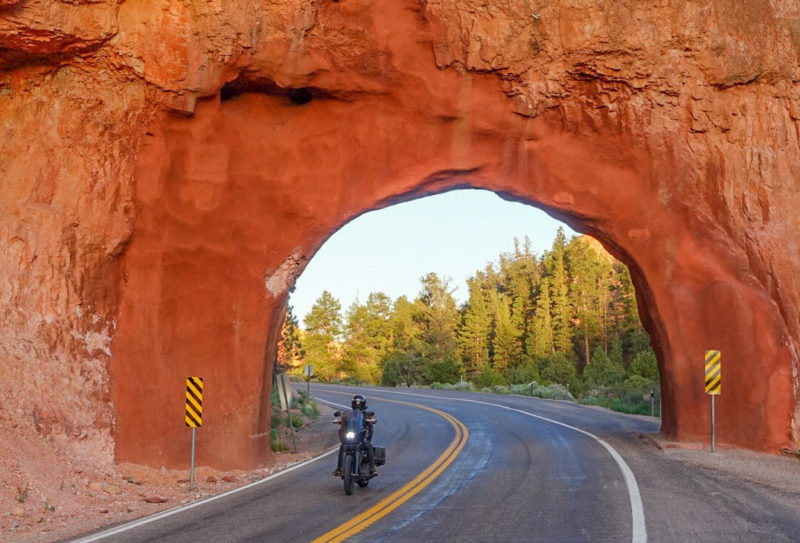 Motorcyclist riding under red rock arch