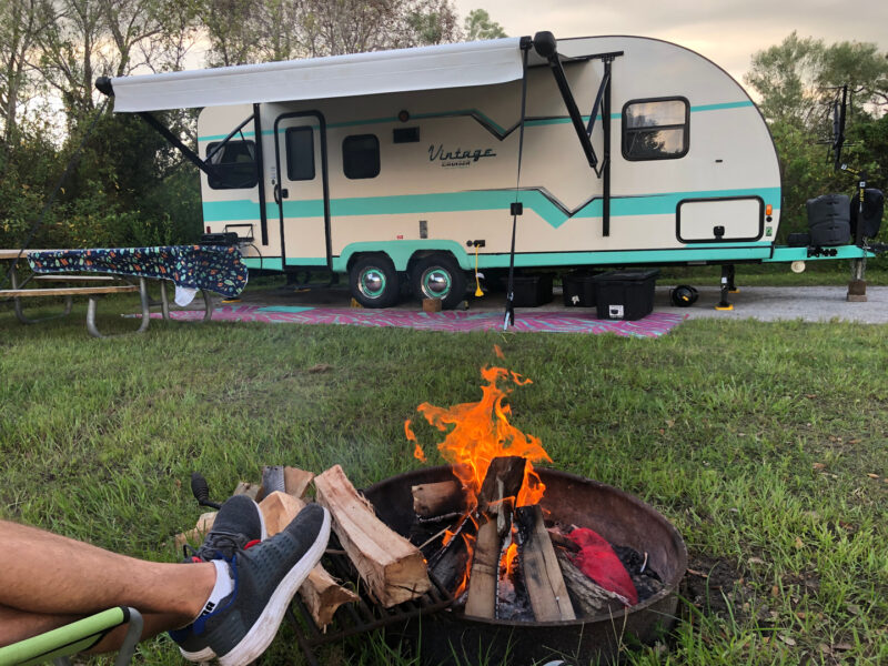 Trailer set up camp in grassy campsite with camper enjoying fire pit