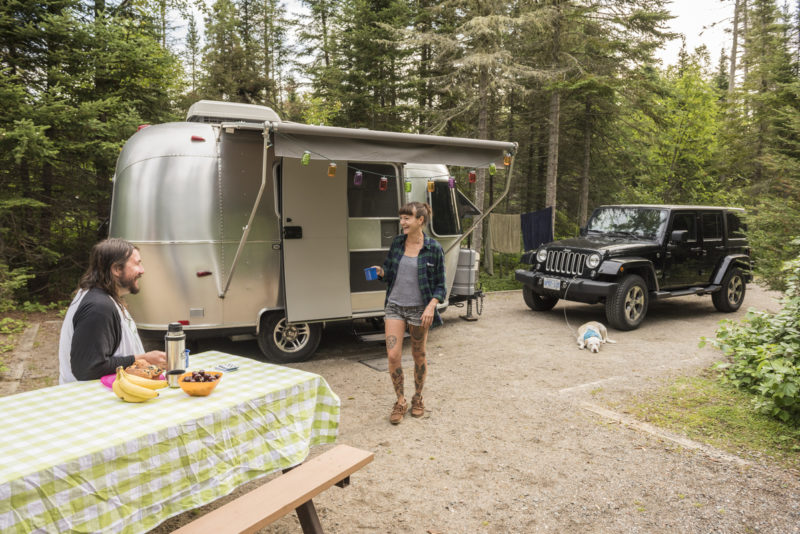 two people at a campground with a silver trailer and black jeep