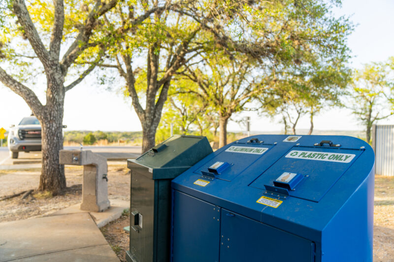 Blue recycling bins and a green trash bin in an outside setting