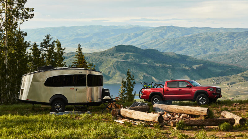 a red pickup truck tows a trailer outside near a campfire and a mountain overlook