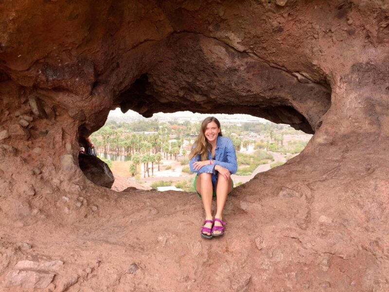 a woman sits and poses in the middle of a hole in a red rock formation