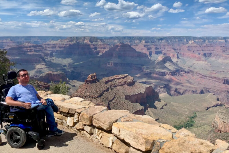 a man in a wheelchair sits at a scenic overlook at the grand canyon