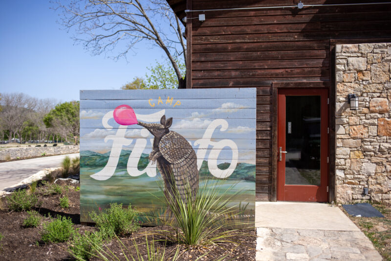 an entrance sign for camp fimfo featuring a handpainted illustration of an armadillo