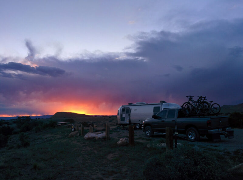 an RV and black pickup truck are parked outside under a sunset