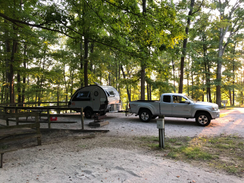 a silver truck with a tear drop trailer is parked at a campground