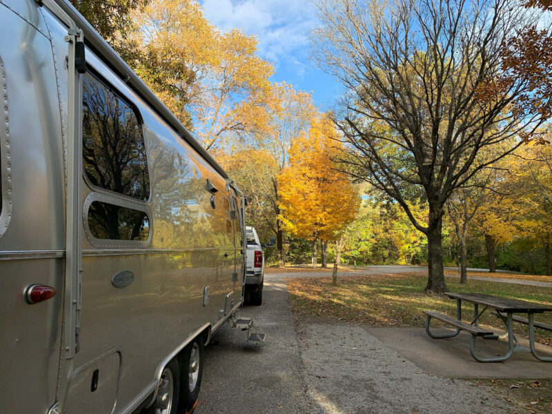 a pickup truck tows a trailer at a campground with fall foliage