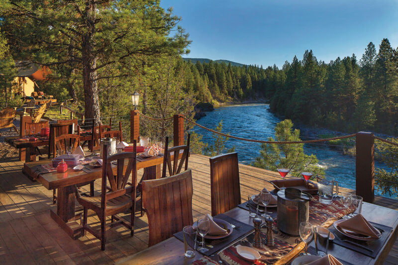 a deck overlooking the water and pine trees with tables set for dinner