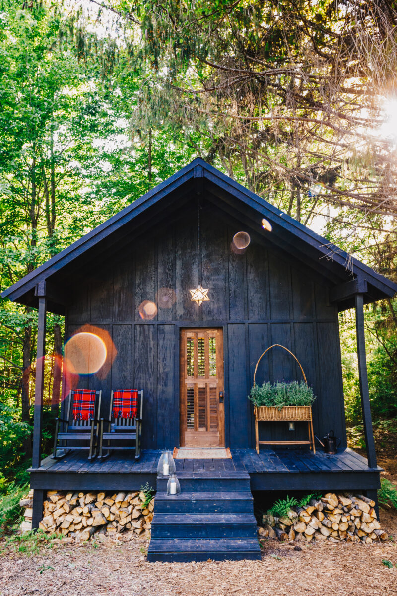 a small wooden cabin in the woods with two rocking chairs on the porch