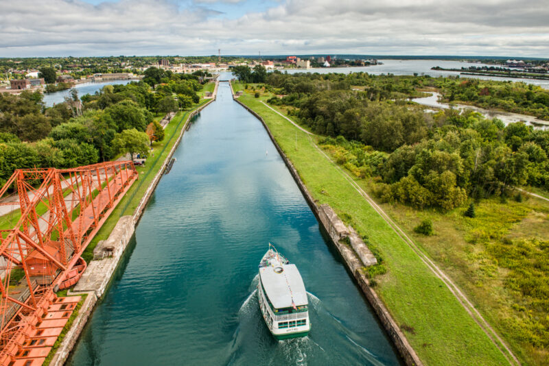 Aerial view of the Sault Ste. Marie Canal with a ship and orange bridge on the shoreline