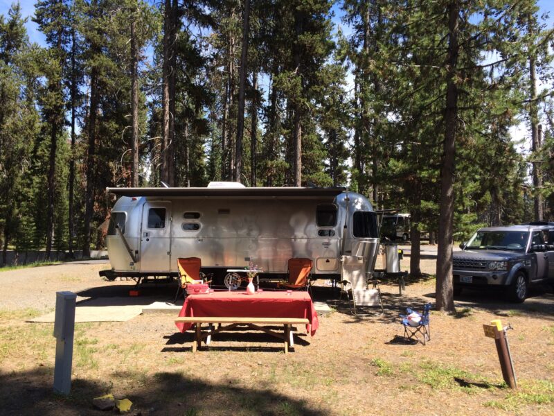 an airstream parked at a campground with two camp chairs and a picnic table