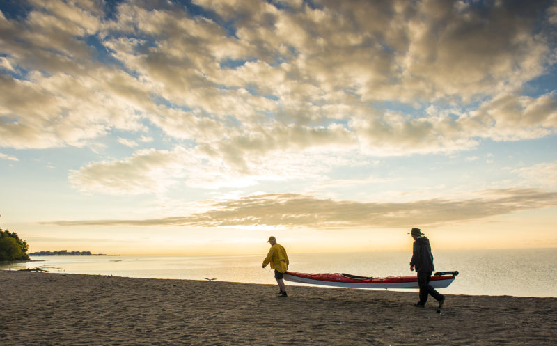 two people carry a kayak near the shore during sunset