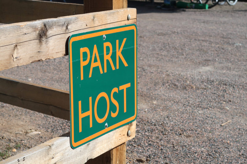 Green and orange sign for park host, hanging on a wooden fence