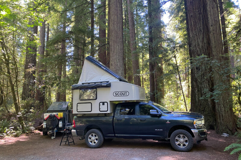a pick up truck with a pop up tent is parked at a wooded campsite