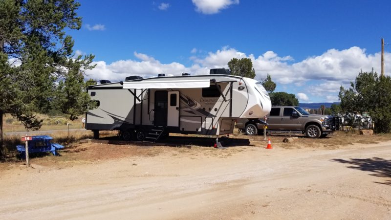 Fifth wheel parked at a campsite on a dirt pad