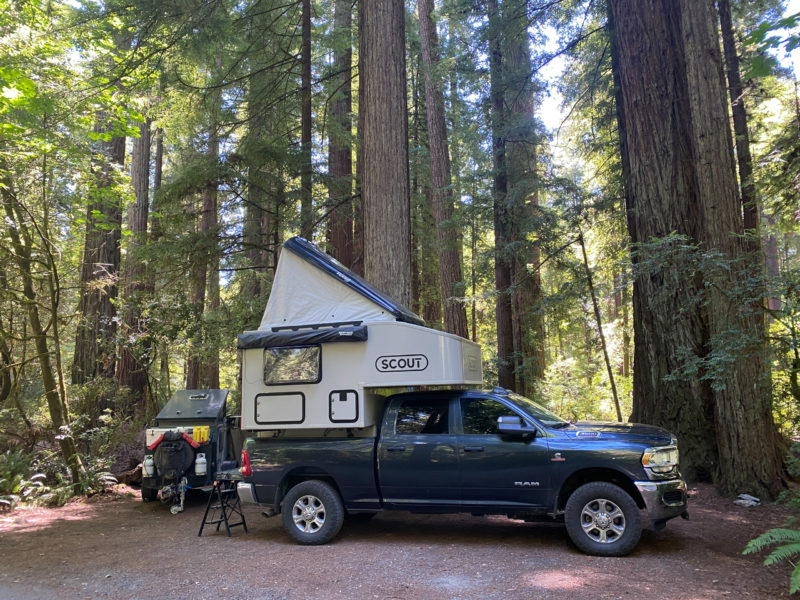 A black pickup truck has a pop up camper parked at a wooded campsite