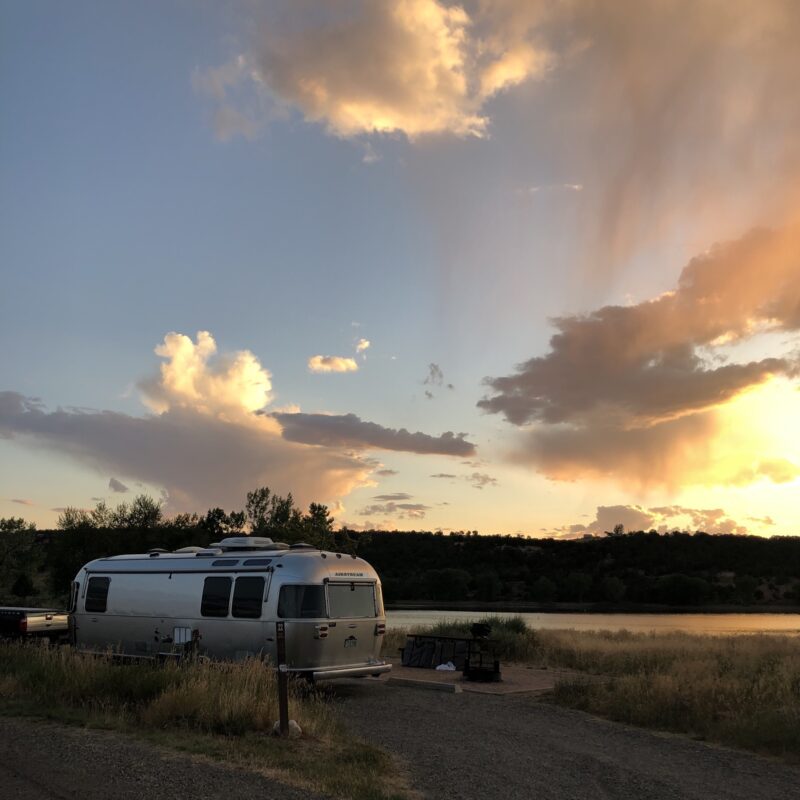 an airstream is parked in nature under a sunset sky