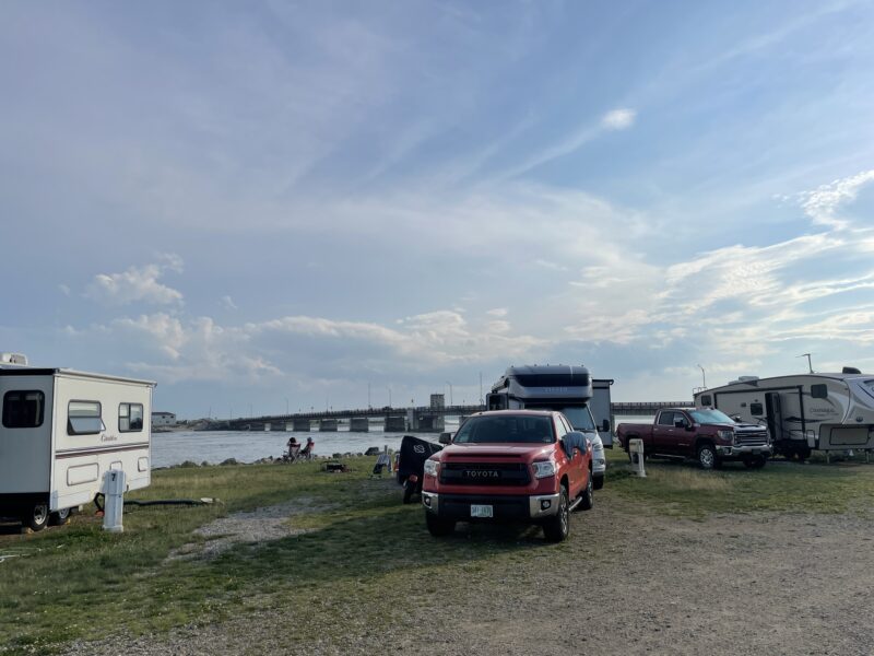 several trucks and rvs are parked at a campsite near the water