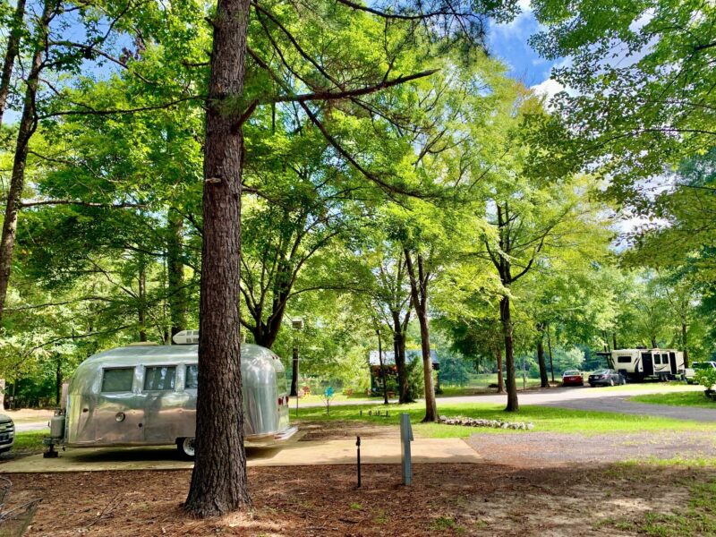 an airstream is parked at a campsite surrounded by greenery