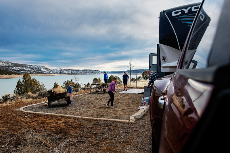 a campsite with an rv and several people next to a body of water with mountains in the background