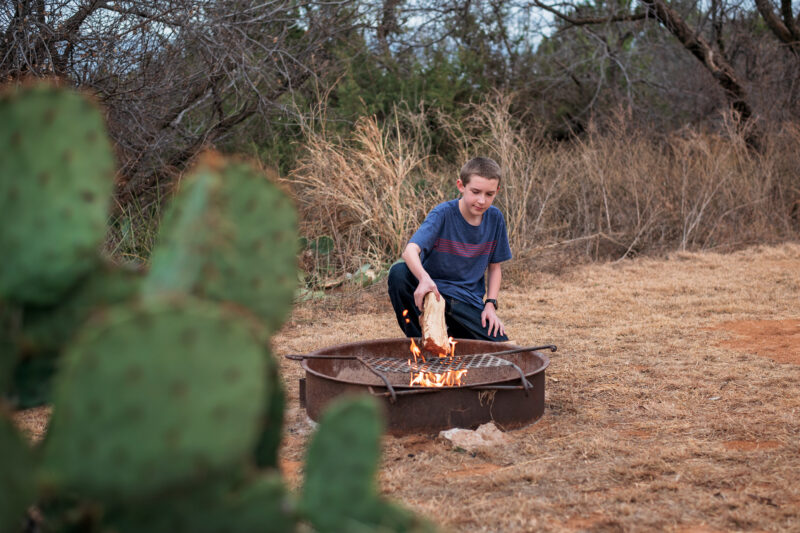 a boy puts a log on a campfire in the desert