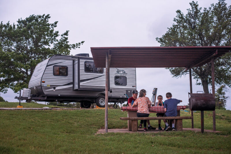 a family eats at a picnic table at a campsite with an rv parked in the background