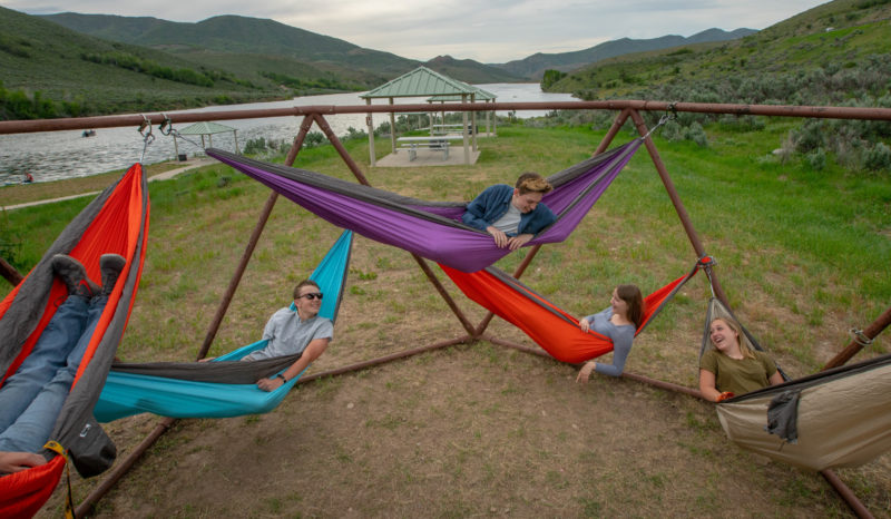 several people lay in colorful hammocks hanging from a metal structure at a campsite
