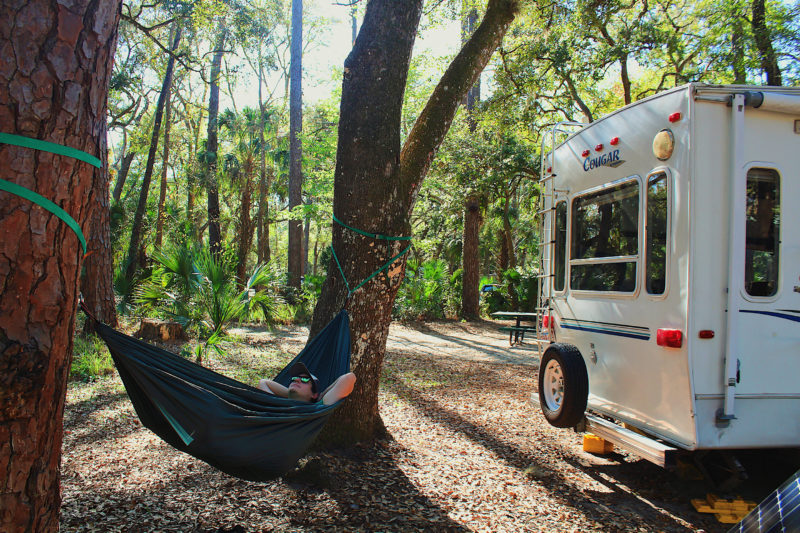 a person lays in a hammock strung between two trees at a campsite next to an rv