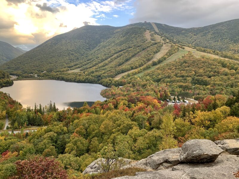 a scenic mountain overlook featuring fall foliage in reds, greens and yellows and a lake
