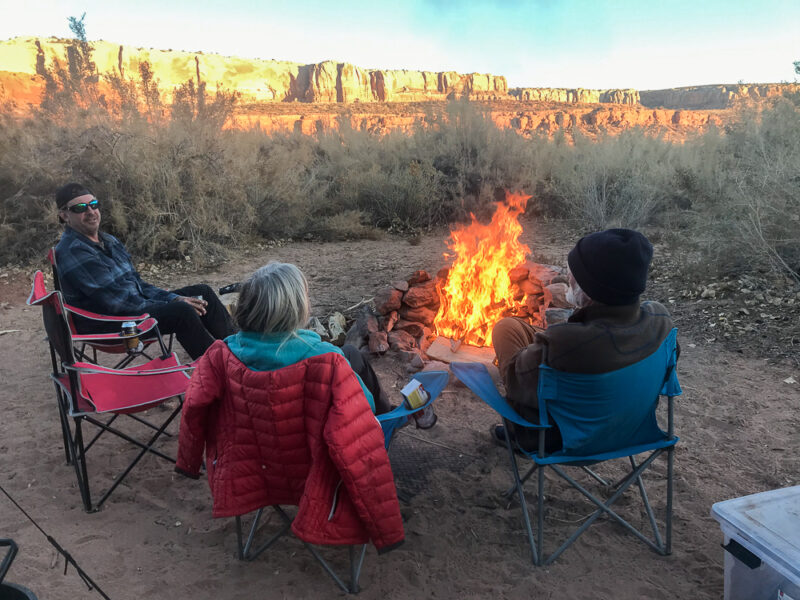 Three people seated in camping chairs around a campfire 