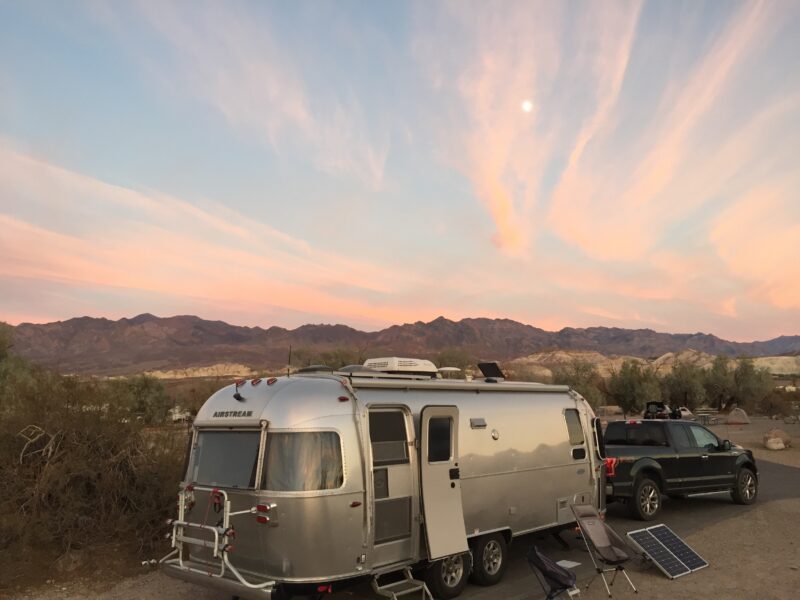 a black truck towing an airstream trailer is parked under a pink and blue sunset sky